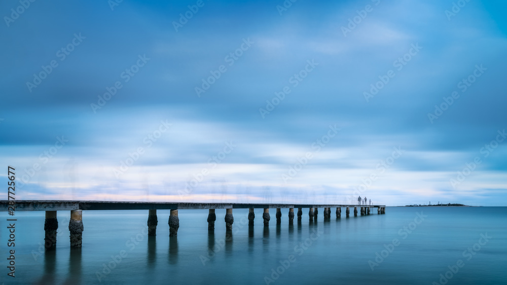 Family journey concept. Long Exposure Image with people walking on the pier at the beach after sunset at Anse Vata Bay, Noumea, New Caledonia in French Polynesia, South Pacific Ocean. 