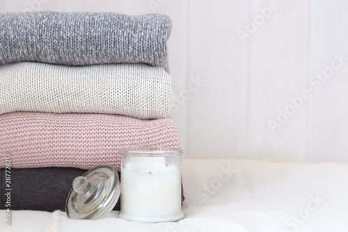 stack of knitted sweaters on a wooden wall background. Scented candles. Cozy warm, rustic-style winter clothes. Stylish casual woolen autumn wardrobe. Hyugge Lagom concept copy space photo