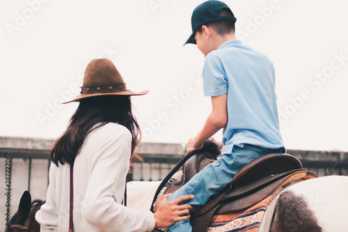 A child with special needs is riding with a close supervision teacher].This is a treatment called Hippotherapy, Life in the education age of disabled children, Happy disability kid concept.