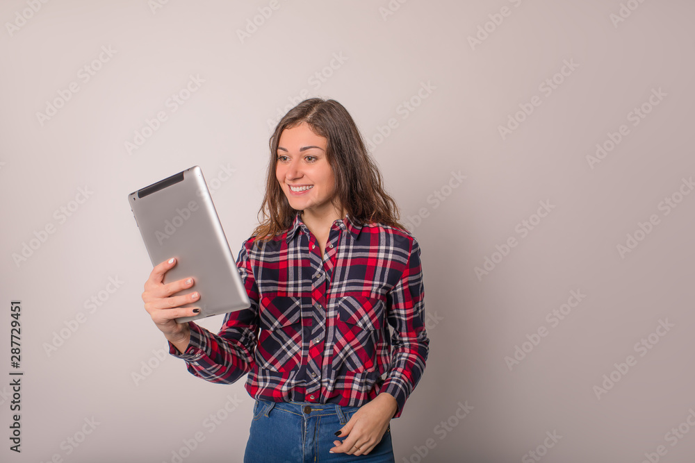 Young stylish happy smiling hipster girl having online video call via portable digital tablet while standing isolated in studio. Cheerful female watching funny video via digital gadget Young stylish happy smiling hipster girl having online video call via portable digital tablet while standing isolated in studio. Cheerful female watching funny video via digital gadget