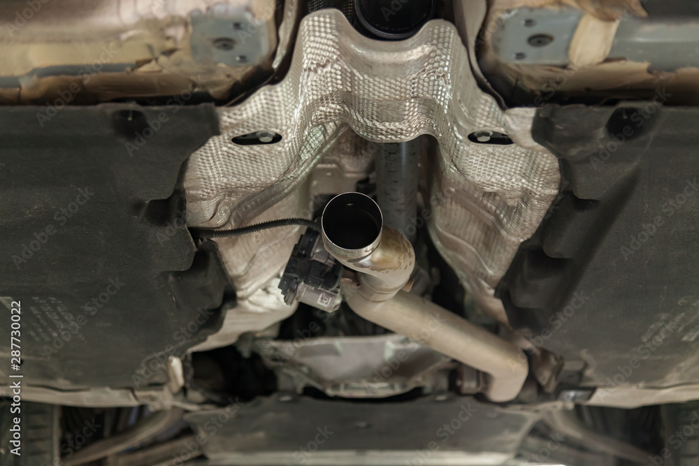 Close-up on the part of the bottom of the car from the front of the exhaust pipe and the catalyst disassembled during the repair in the workshop auto service vehicles Close-up on the part of the bottom of the car from the front of the exhaust pipe and the catalyst disassembled during the repair in the workshop auto service vehicles