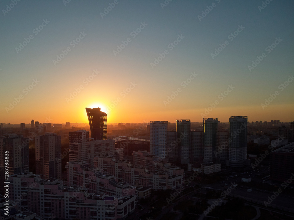 Fototapeta premium Sun is setting behind tower. Evening cityscape. Aerial view