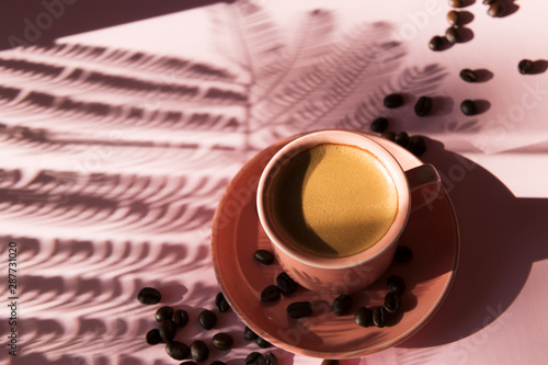 Coral colored cup with effuse coffee's beans with shadows on pastel rose background. Flat lay. Top view. Coffee concept. Pop art still life photo