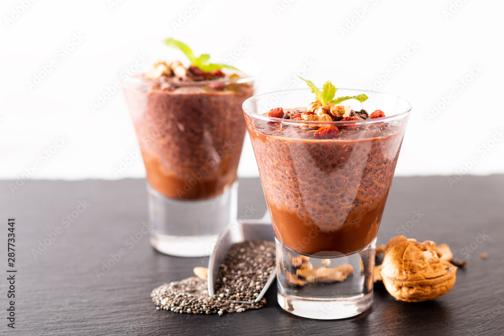 Healthy food concept Chia seeds, chocolate milk pudding with goji and dried walnuts in small Glass on black slate board background Healthy food concept Chia seeds, chocolate milk pudding with goji and dried walnuts in small Glass on black slate board background