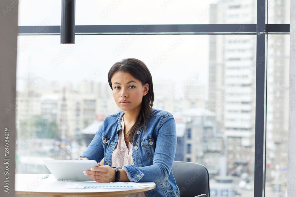 Portrait of young businesswoman in casual clothing sitting at the table and working with digital tablet at office Portrait of young businesswoman in casual clothing sitting at the table and working with digital tablet at office
