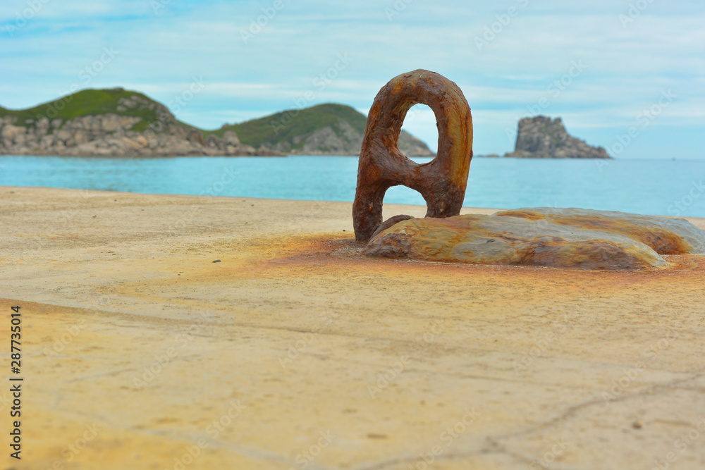 Fototapeta premium Large rusty noose on a concrete pier, turquoise sea and green islands on the horizon