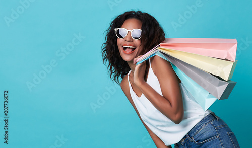 Portrait of an excited young african woman hand holding shopping bag isolated over blue background. photo