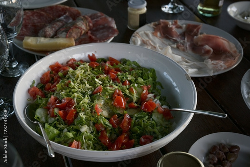 Mediterranean salad of lettuce, tomatoes and cucumbers on a rustic covered table at an outdoor dinner © Maren Winter