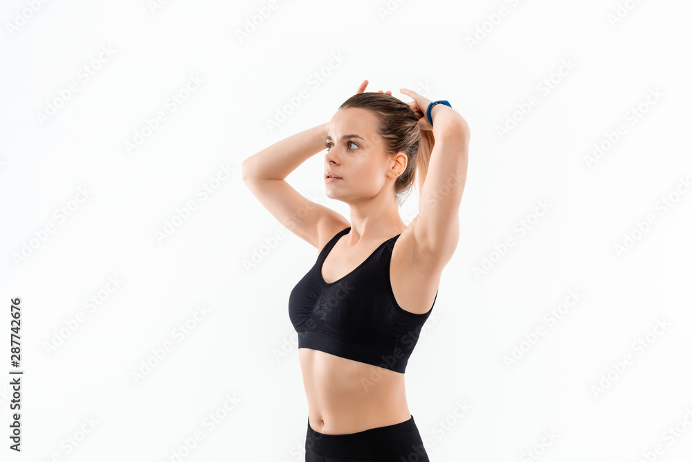 Obraz premium Pretty young sporty blond woman in a black sportswear fixes hair before exercising isolated over white background.