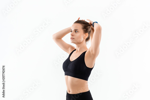 Pretty young sporty blond woman in a black sportswear fixes hair before exercising isolated over white background.