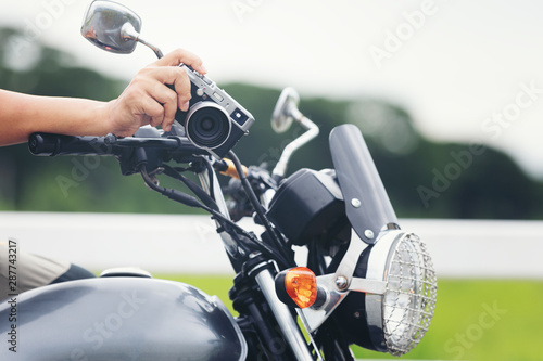 Young Asian male traveler and photographer sitting on the classic style racer motorbike holding camera taking photo on road ,Travel photography concept