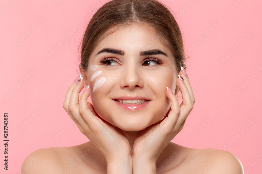 Excited beautiful model looks at the camera isolated over pink background. Moisturizing hyaluronic cream applied to skin. Concept of beauty and health treatment. Excited beautiful model looks at the camera isolated over pink background. Moisturizing hyaluronic cream applied to skin. Concept of beauty and health treatment.