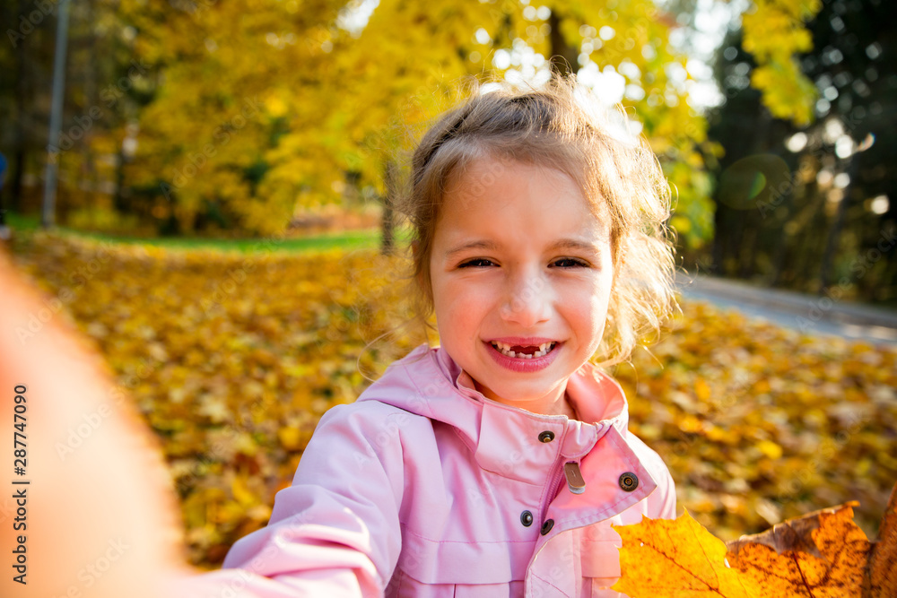 Cute little girl with missing teeth taking selfie. Happy child laughing and smiling. Sunny autumn forest, sun beam. Cute little girl with missing teeth taking selfie. Happy child laughing and smiling. Sunny autumn forest, sun beam.