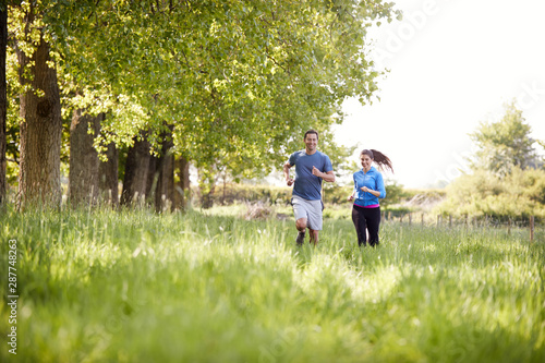 Couple Exercising Running Through Countryside Field Together