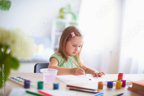 joyful girl child draws gouache in different colors on a white sheet of paper.