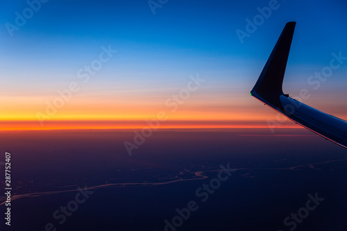 Beautiful sunrise sky above clouds with aircraft wing. View from airplane window