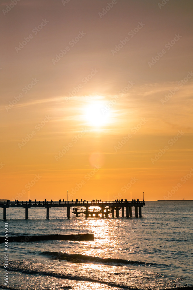 silhouettes of people walking on a pier by the sea against a sunset orange sky silhouettes of people walking on a pier by the sea against a sunset orange sky
