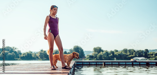 Obraz na plátně Girl standing on the dock with dog by the river