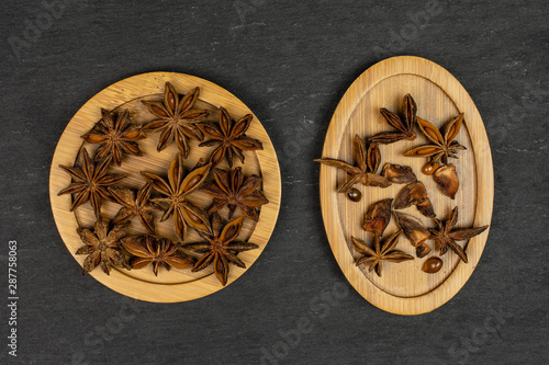 Lot of whole lot of pieces of dry brown star anise illicium verum on round bamboo coaster on oval bamboo coaster flatlay on grey stone photo