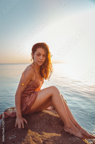 Beautiful woman in lingerie posing on a coastal cliff. Sea and sunset in the background. Vertical orientation © _KUBE_
