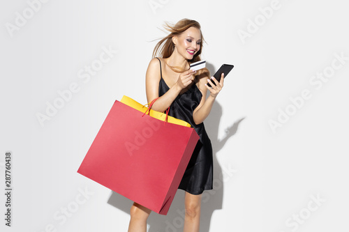 Young blonde woman in black dress shopping on white background. Attractive caucasian female model. Finance, black friday, cyber monday, sales, autumn concept. Copyspace. Online payments bill.