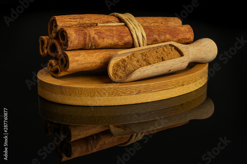 Group of six whole dry brown cinnamon wrapped in natural twine in a wooden scoop on oval bamboo coaster isolated on black glass photo