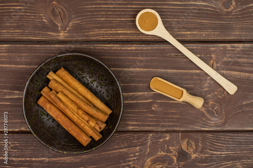 Lot of whole dry brown cinnamon in dark ceramic bowl in a wooden spoon in a wooden scoop flatlay on brown wood photo