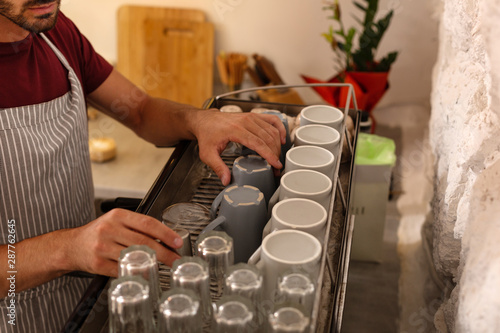 Fotografie Bearded hard-working barista putting cups after washing