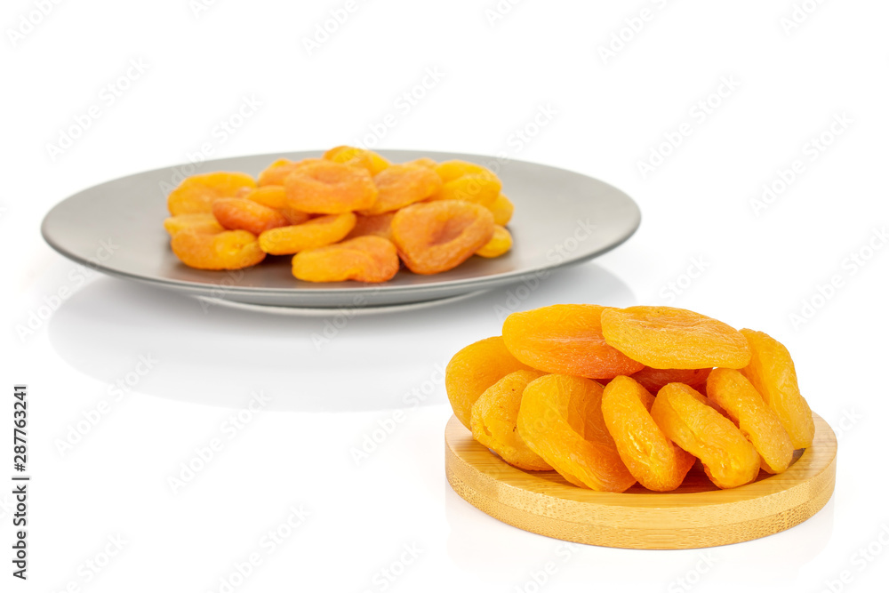 Lot of whole dried orange apricot on round bamboo coaster on gray ceramic plate isolated on white background Lot of whole dried orange apricot on round bamboo coaster on gray ceramic plate isolated on white background