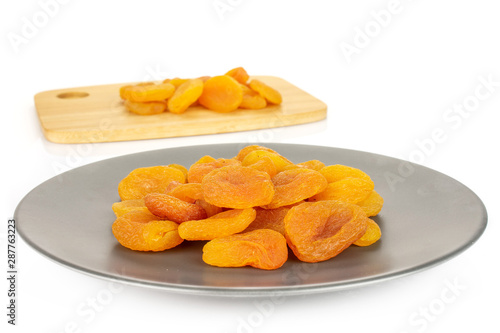 Lot of whole dried orange apricot on bamboo cutting board on gray ceramic plate isolated on white background