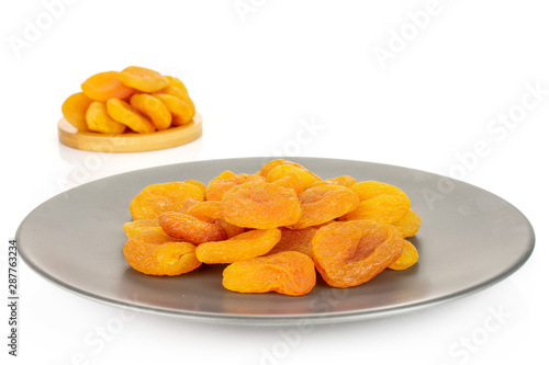 Lot of whole dried orange apricot on round bamboo coaster on gray ceramic plate isolated on white background