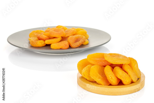 Lot of whole dried orange apricot on round bamboo coaster on gray ceramic plate isolated on white background