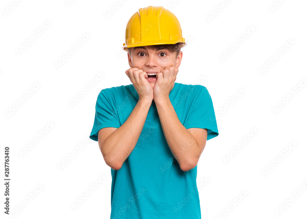 Unhappy teen boy wearing yellow hard hat looking stressed and nervous with hands on mouth biting nails. Child gnaws his nails for fear, afraid of punishment. Young teenager in helmet looking at camera Unhappy teen boy wearing yellow hard hat looking stressed and nervous with hands on mouth biting nails. Child gnaws his nails for fear, afraid of punishment. Young teenager in helmet looking at camera
