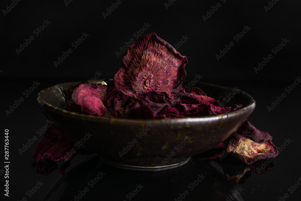 Obraz premium Lot of slices of dried red beetroot in dark ceramic bowl isolated on black glass