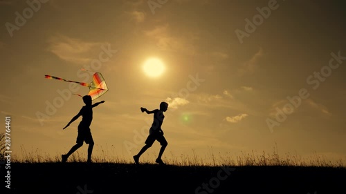 Happy family playing outdoors, flying kite flying. Silhouette of children with a kite at sunset. Team work, team play outdoor games