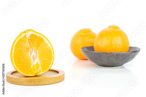 Group of two whole one half of fresh orange tangelo minneola in dark ceramic bowl on round bamboo coaster isolated on white background