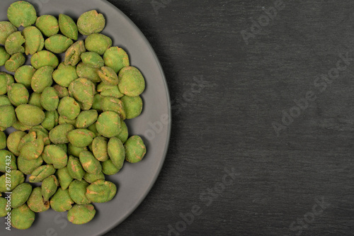 Lot of whole spicy green wasabi peanut on gray ceramic plate flatlay on grey stone