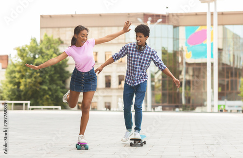 Happy teenage couple riding modern cruiser skateboards on city street