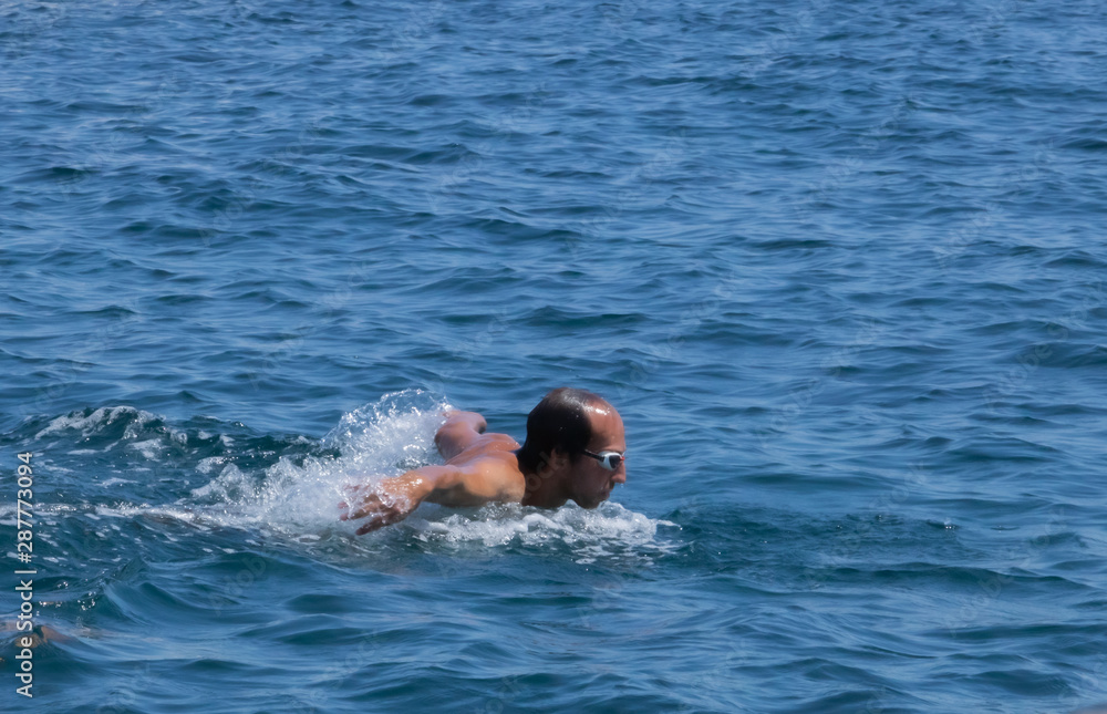 Homme nageant la nage papillon en pleine mer, tête sortie de l'eau pour reprendre son souffle