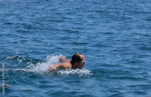 Homme nageant la nage papillon en pleine mer, tête sortie de l'eau pour reprendre son souffle