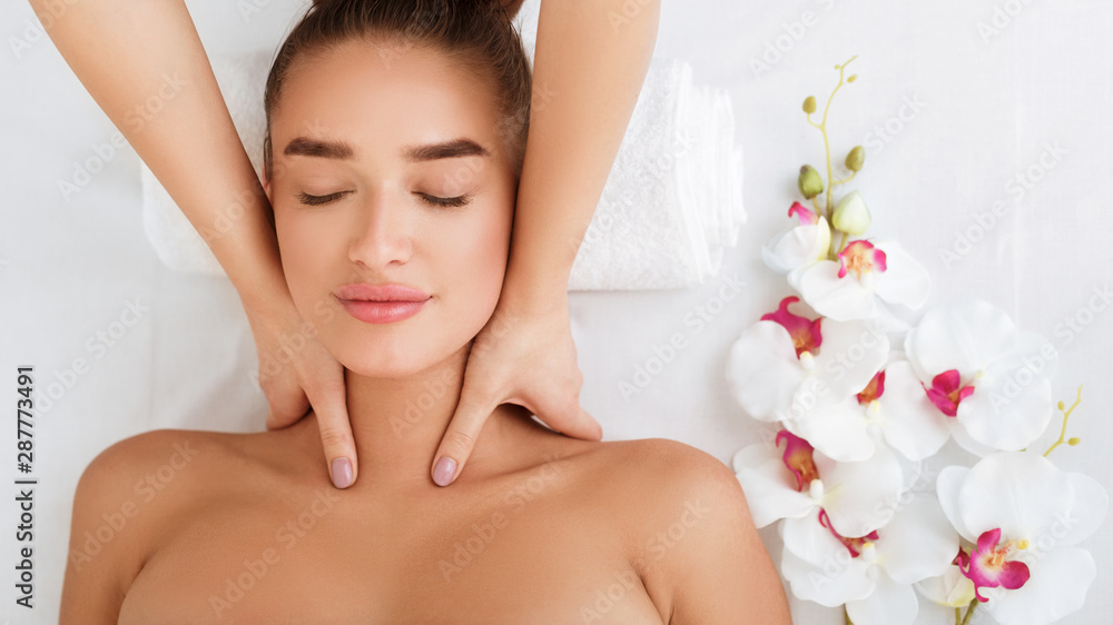 Woman getting neck massage, relaxing with orchid flowers nearby Woman getting neck massage, relaxing with orchid flowers nearby