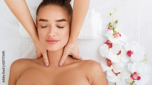 Woman getting neck massage, relaxing with orchid flowers nearby
