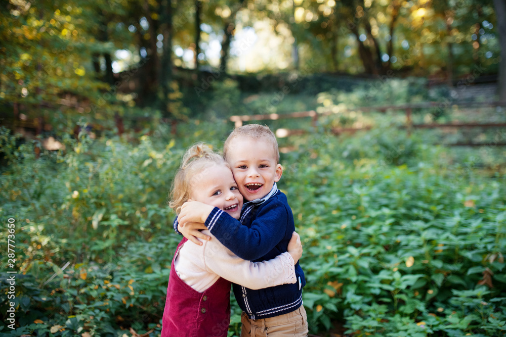 Fototapeta premium Twin toddler sibling boy and girl standing in autumn forest, hugging.