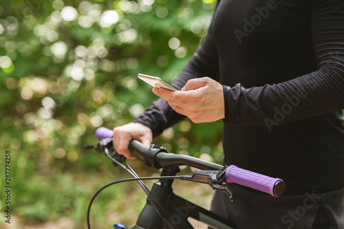 Close up of cyclist holding bike and using phone