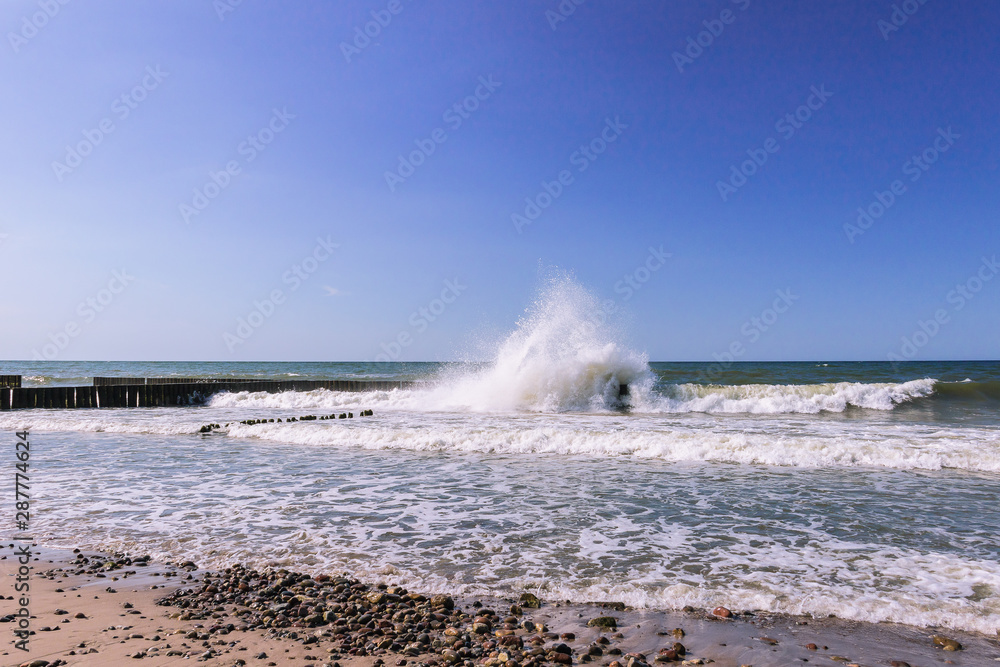 Seascape with waves crashing the wooden poles breakwater on a sunny 