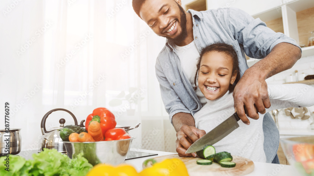 Father and daughter cutting cucumber together and smiling