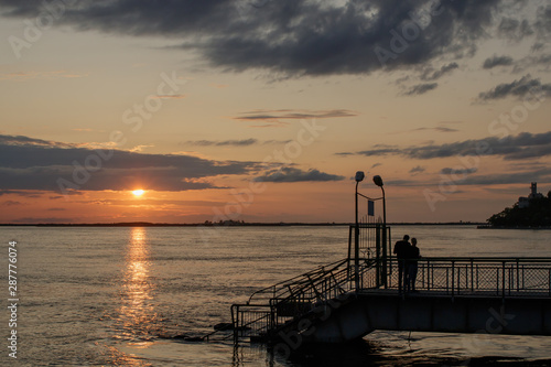 Sunset on the Amur River. The silhouettes of the pier and 2 young men standing on it are visible.