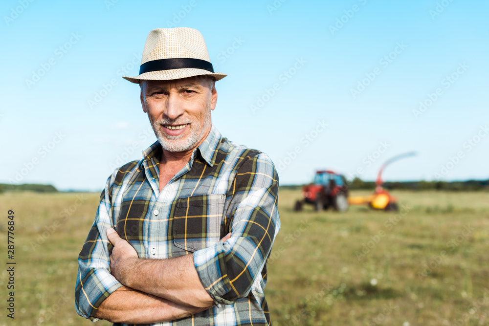 happy senior farmer standing with crossed arms in field happy senior farmer standing with crossed arms in field