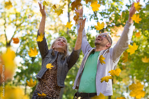 Loving couple in the autumn park. Spouses of middle age for a walk.Men and women throw yellow leaves
