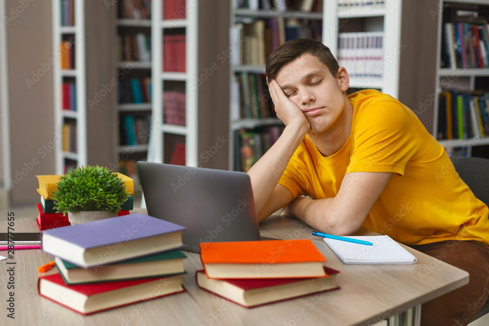 Male student sleeping at workplace in college library Male student sleeping at workplace in college library